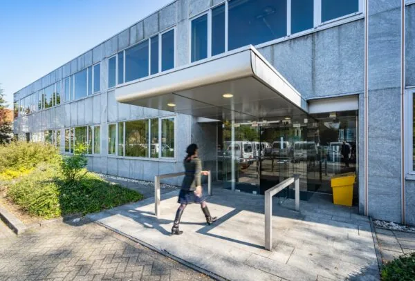 Ingang van een modern kantoorgebouw aan de Utrechtseweg met een wandelende persoon op de voorgrond.