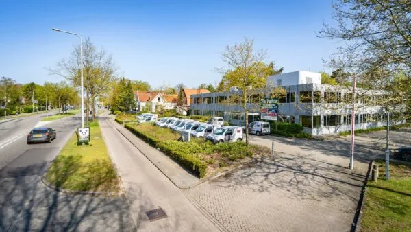 Kantoorpand aan de Utrechtseweg in een groene omgeving met geparkeerde bedrijfsauto’s en langsrijdend verkeer.