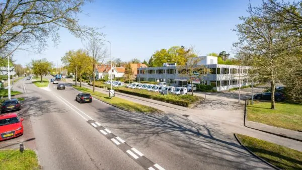 Kantoorpand met parkeerplaats aan de Utrechtseweg in Arnhem, gezien vanaf de overkant van de weg op een zonnige dag.