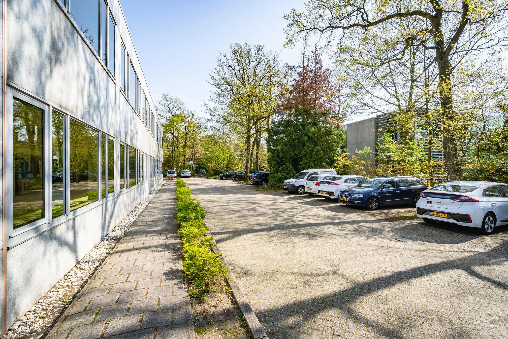 Parkeerterrein met geparkeerde auto's naast een kantoorgebouw aan de Utrechtseweg, omringd door bomen.