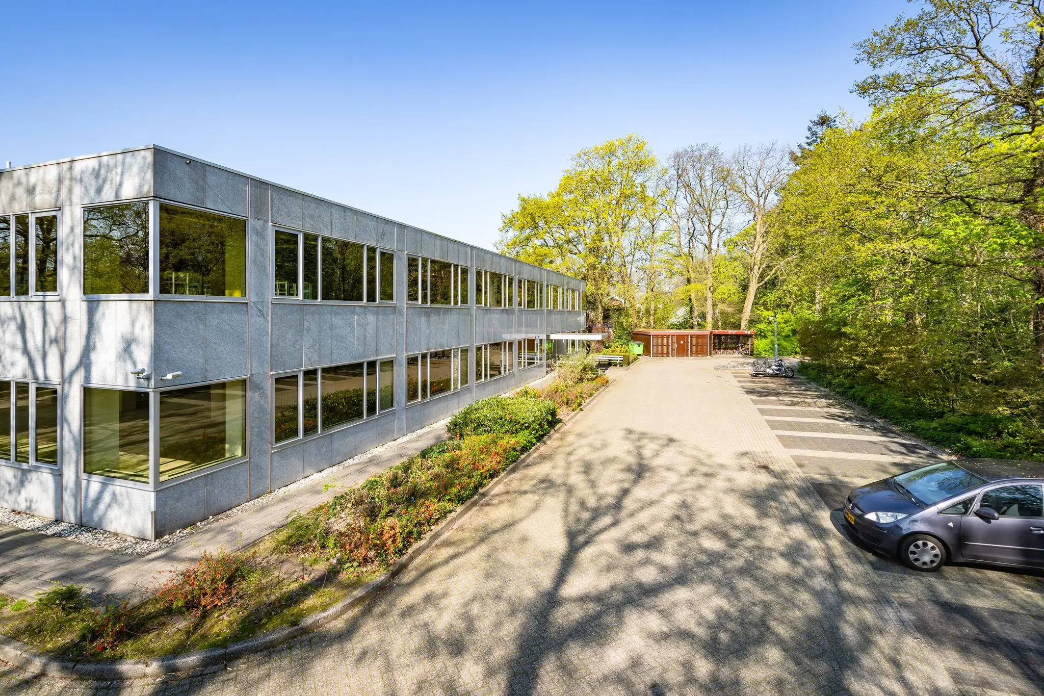 Modern kantoorgebouw aan de Utrechtseweg met omliggende parkeerplaatsen en groene, bosrijke omgeving.
