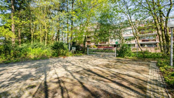 Gedeeltelijk met bomen omgeven parkeerterrein aan de Utrechtseweg met zicht op een appartementencomplex en toegangspoort.