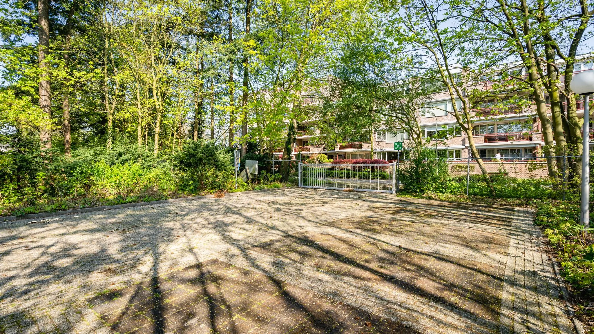 Gedeeltelijk met bomen omgeven parkeerterrein aan de Utrechtseweg met zicht op een appartementencomplex en toegangspoort.