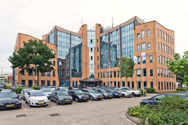 Kantoorpand aan het Kosterijland met een glazen gevel en volle parkeerplaats op de voorgrond.