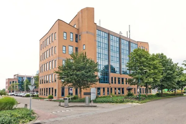 Modern kantoorgebouw aan het Kosterijland met grote ramen en omringd door groen.