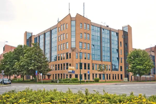 Kantoorgebouw aan het Kosterijland met oranje bakstenen en grote glazen ramen, gelegen aan een rotonde met groenvoorziening.