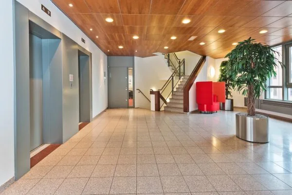 Moderne, lichte entreehal in kantoorpand Kosterijland met liften, trap, rode zitplaatsen en grote kamerplanten.