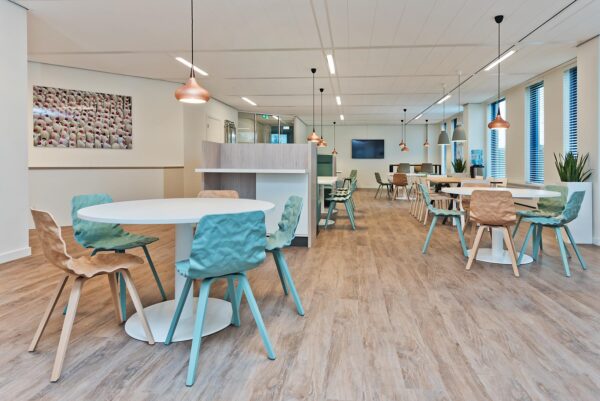 Moderne en open kantoorkantine met ronde tafels, gekleurde stoelen en warme verlichting op Kosterijland.