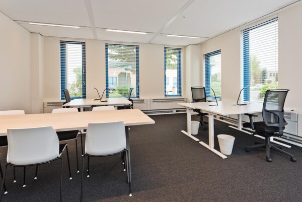 Moderne en lichte kantoorruimte aan het Kosterijland met meerdere bureaus, stoelen en grote ramen met jaloezieën.