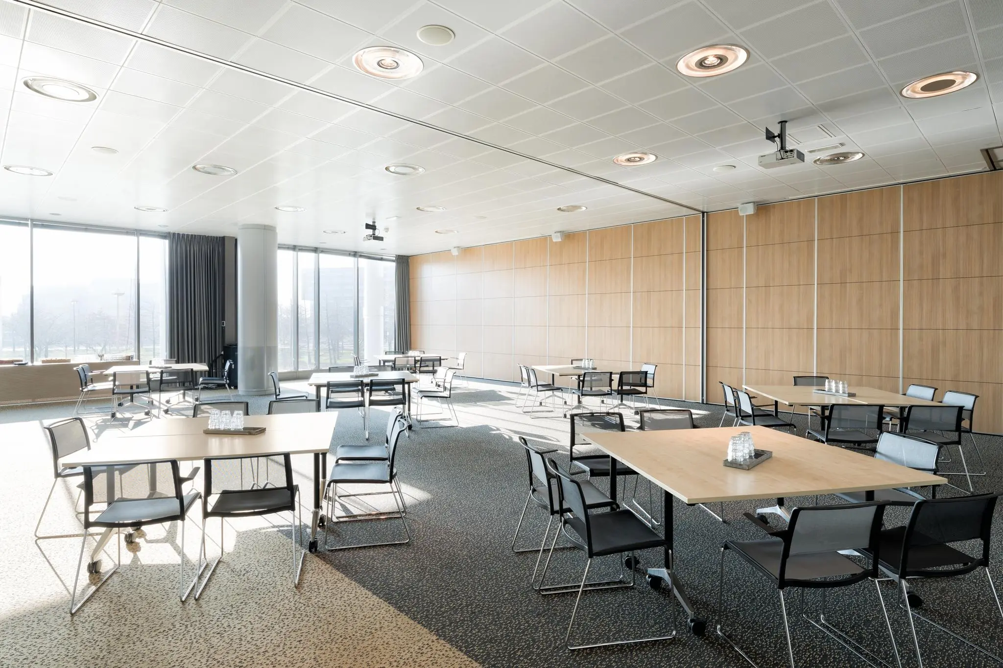 Lichtovergoten vergaderruimte aan de Mercatorlaan met verrijdbare tafels, zwarte stoelen en grote ramen.