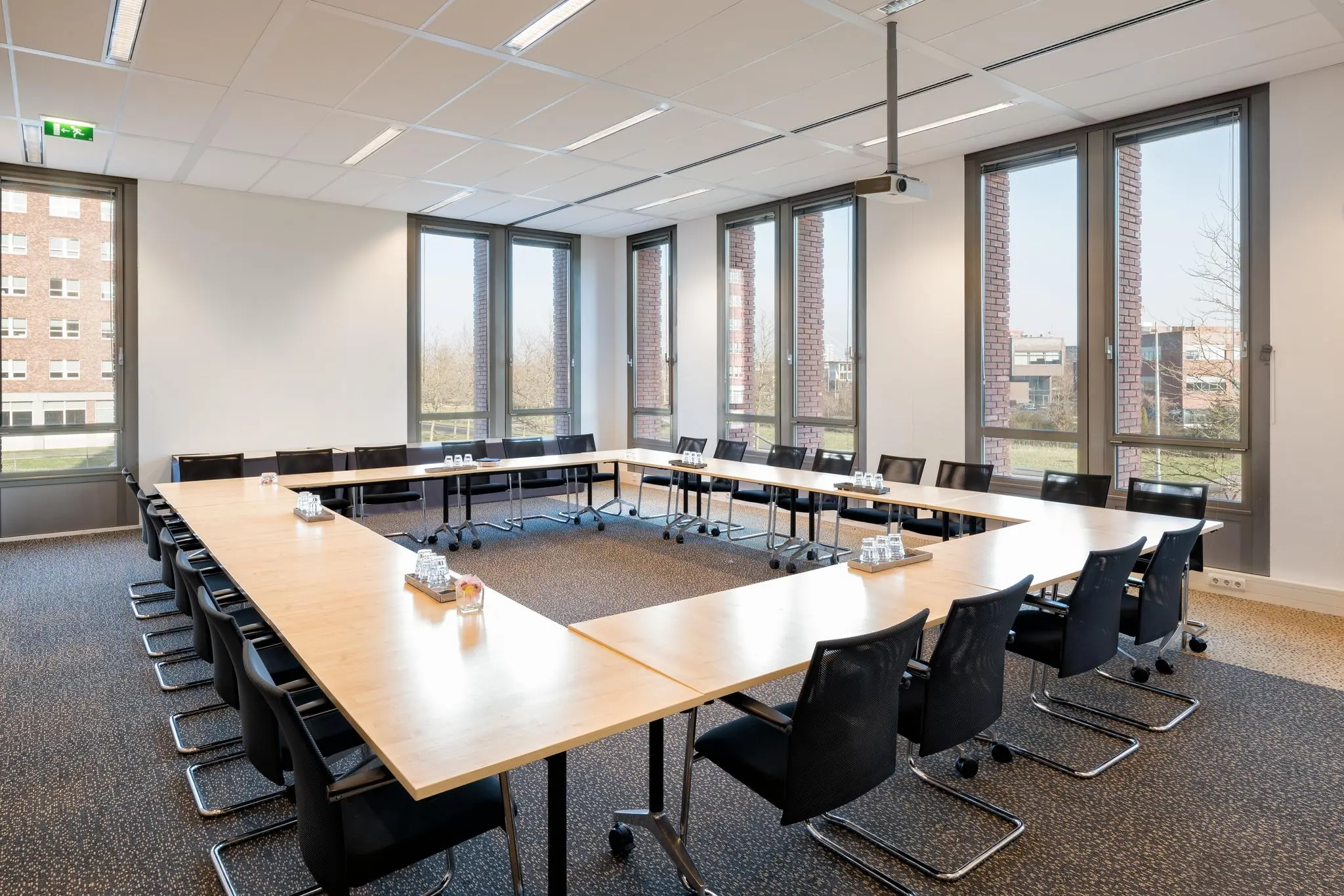 Vergaderruimte aan de Mercatorlaan met U-vormige opstelling, moderne stoelen en grote ramen met uitzicht op kantoorgebouwen.