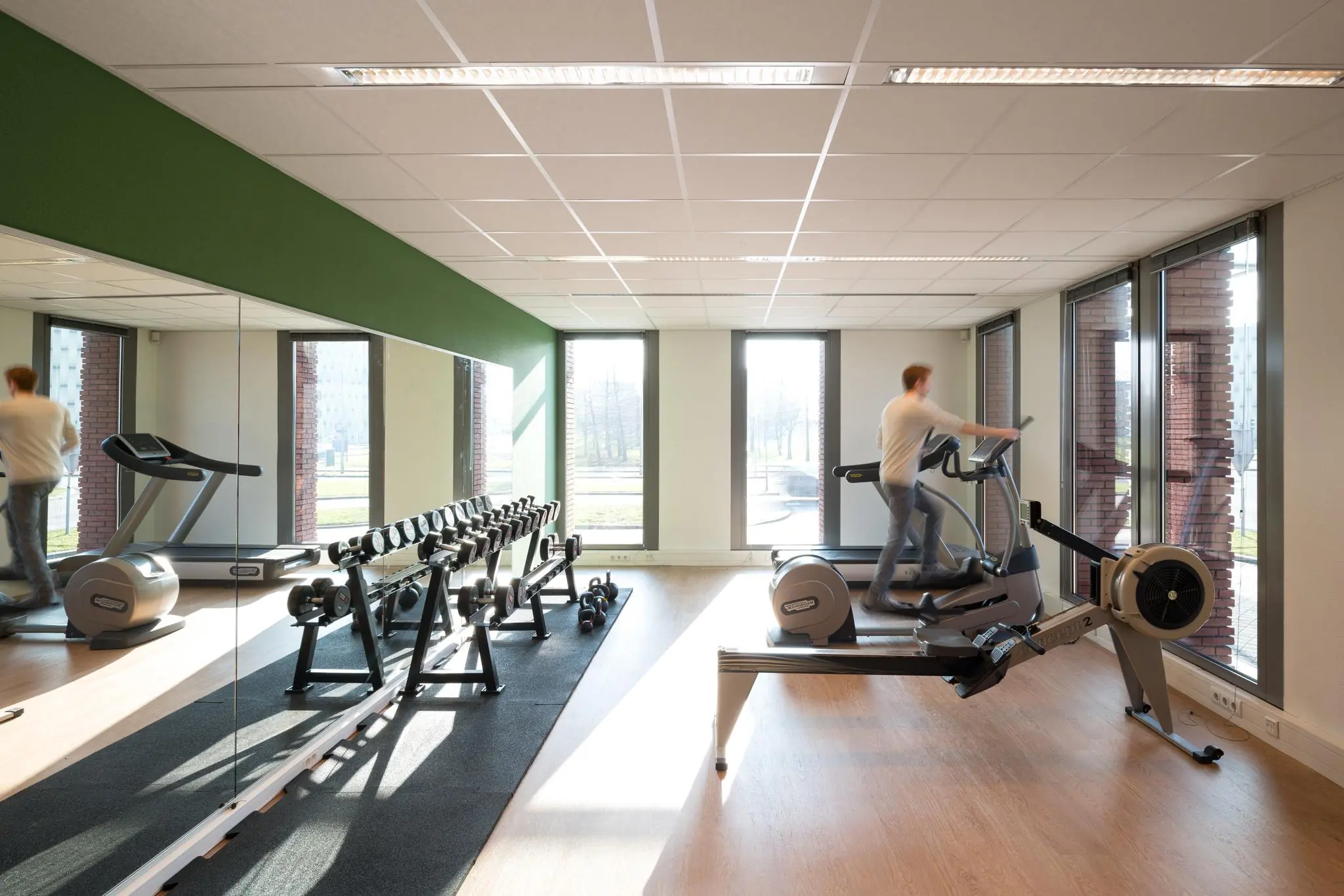 Moderne fitnessruimte aan de Mercatorlaan met cardiotoestellen, halters en grote ramen met daglicht.