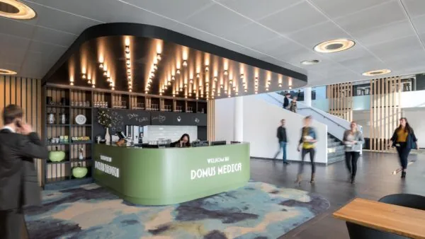 Ontvangstbalie van Domus Medica met moderne inrichting en passerende bezoekers in een open, licht atrium.