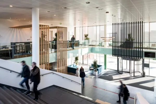 Moderne, lichte entreehal van een kantoorgebouw aan de Mercatorlaan met glazen wanden, houten accenten en meerdere mensen in beweging.