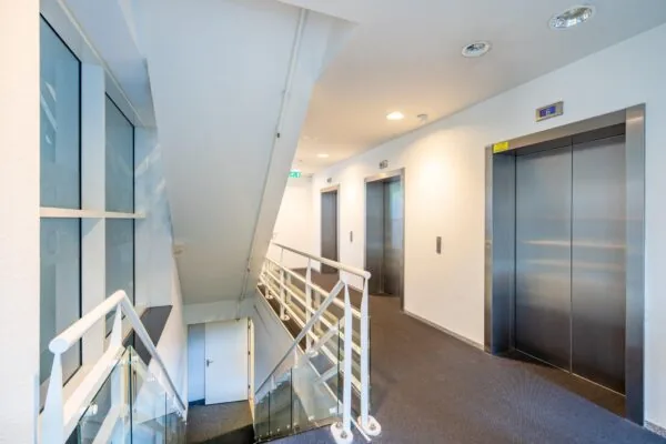 Moderne gang met twee liften, trap en glazen balustrade in het kantoorgebouw aan de Newtonlaan.