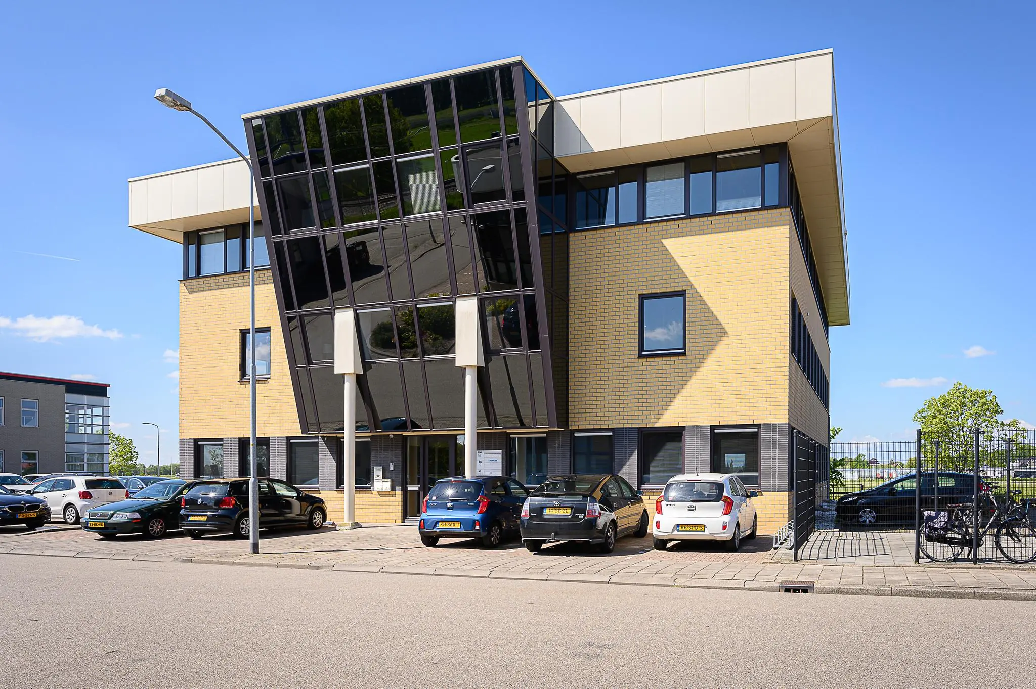 Modern kantoorgebouw aan de Spoorhaven met gele bakstenen en grote, schuine glazen gevel.