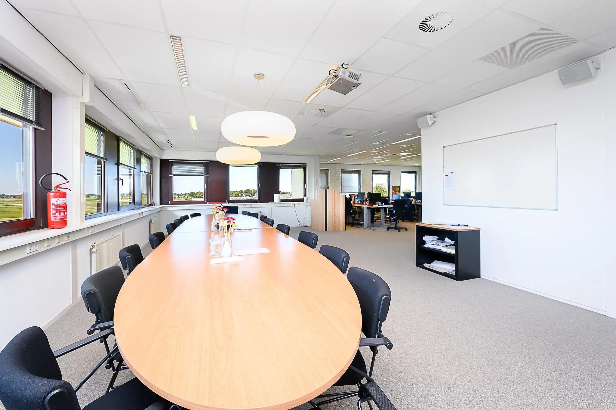 Vergaderruimte met lang ovale tafel, zwarte stoelen en uitzicht op een groen landschap in kantoorpand Spoorhaven.