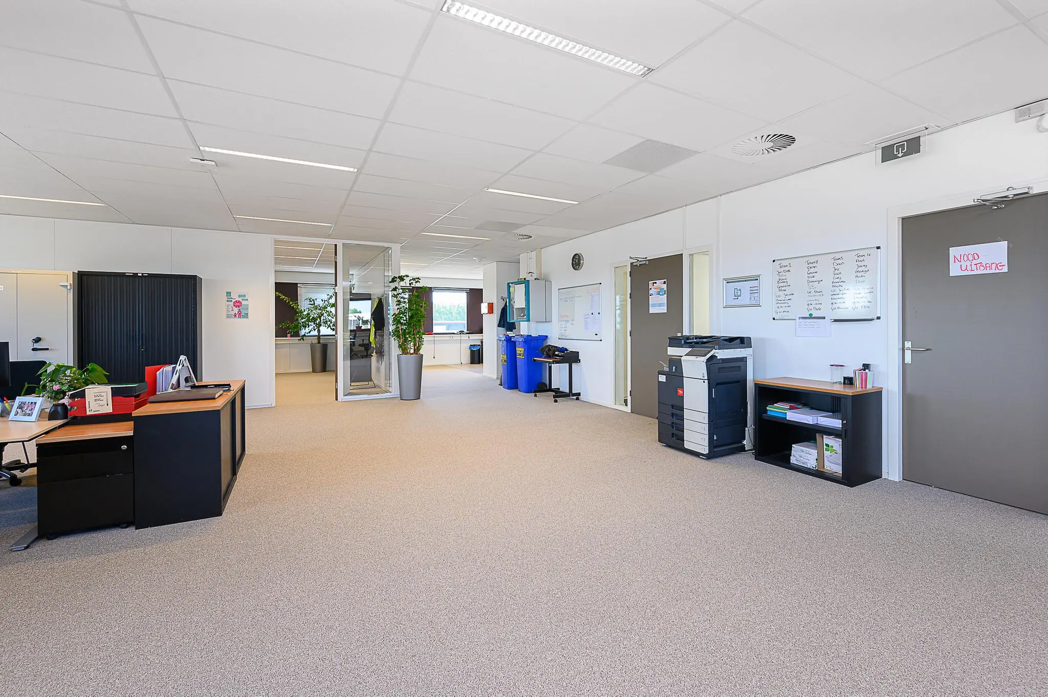 Moderne en ruime kantoorgang met bureaus, planten, printers en recyclebakken in het gebouw Spoorhaven.
