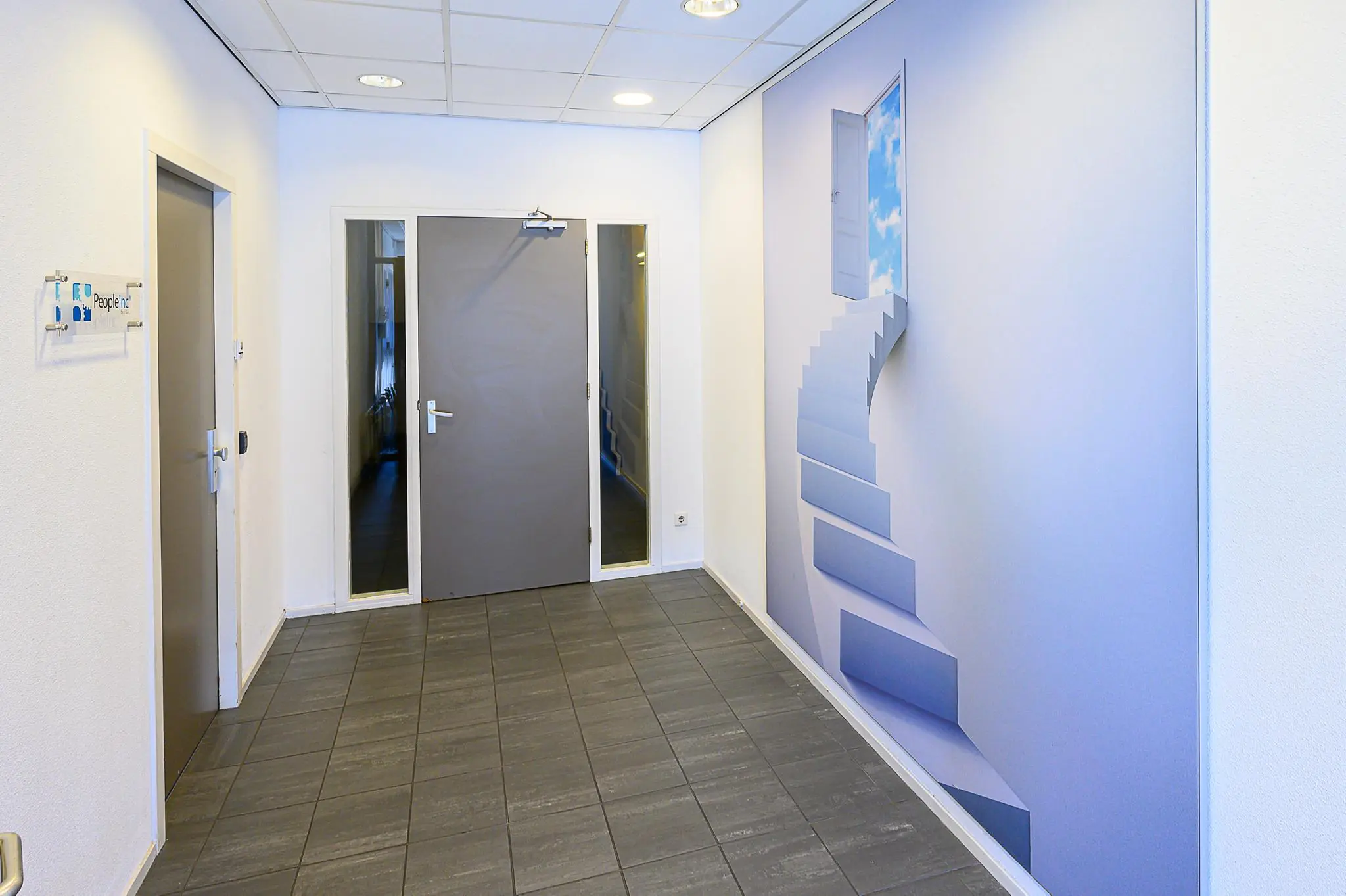 Hal met grijze deuren en een muurschildering van een wenteltrap naar een open deur in de lucht.