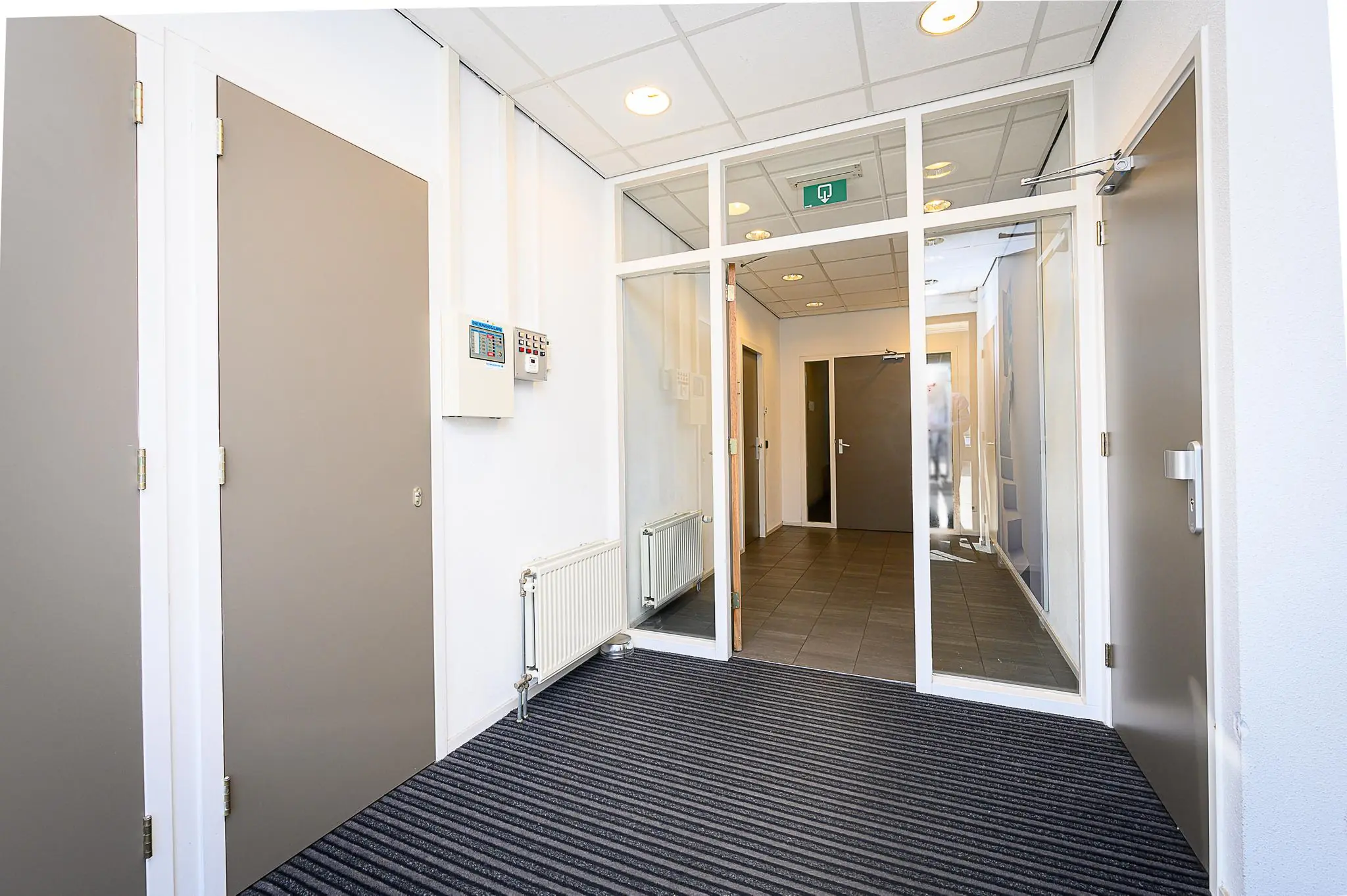 Heldere hal met grijze deuren, glazen scheidingswand en veiligheidssysteem in een kantoorpand aan de Spoorhaven.