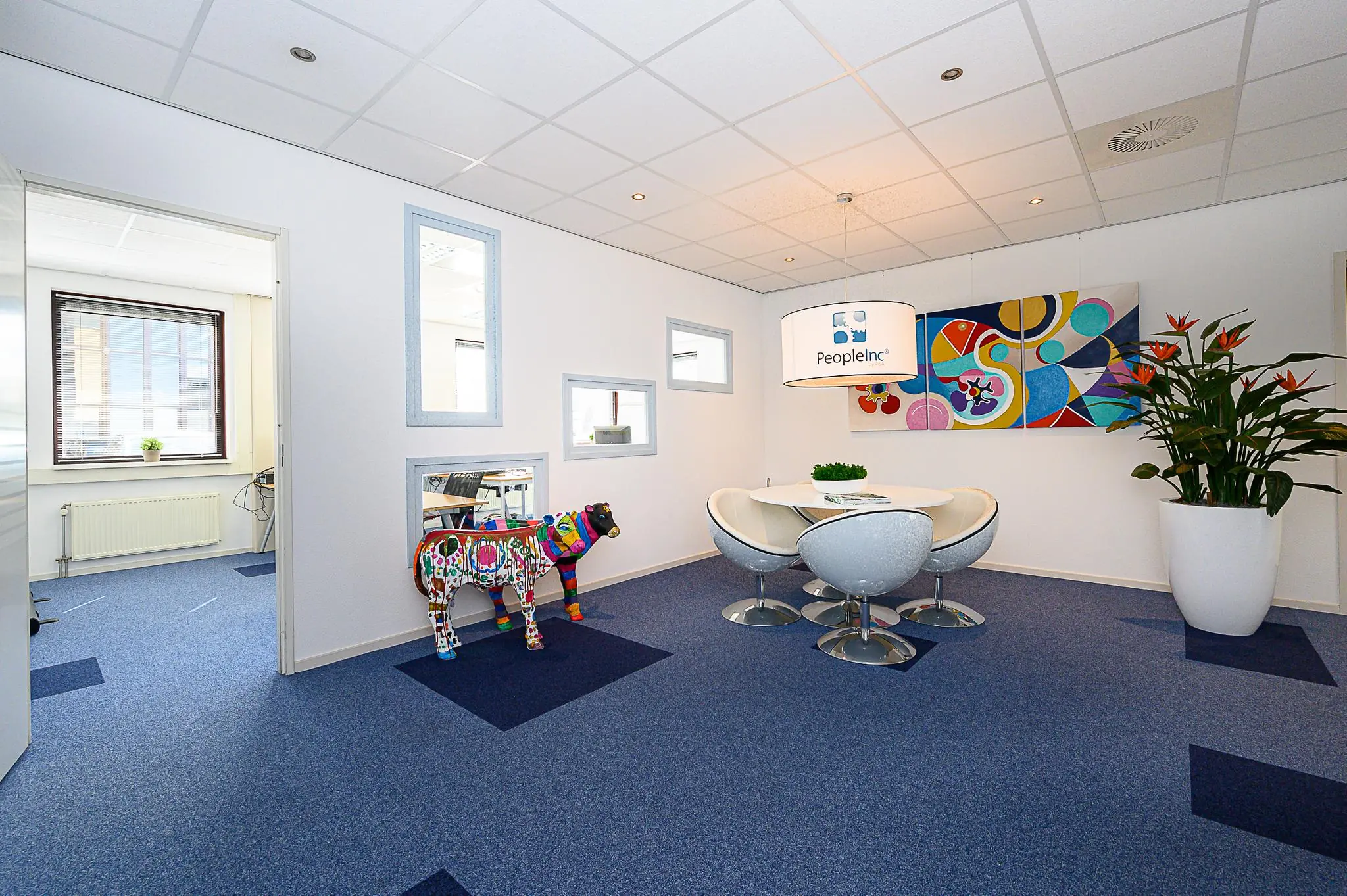 Moderne kantoorruimte van PeopleInc met ronde vergadertafel, kleurrijke kunst en decoratief beeld van een beschilderde koe.