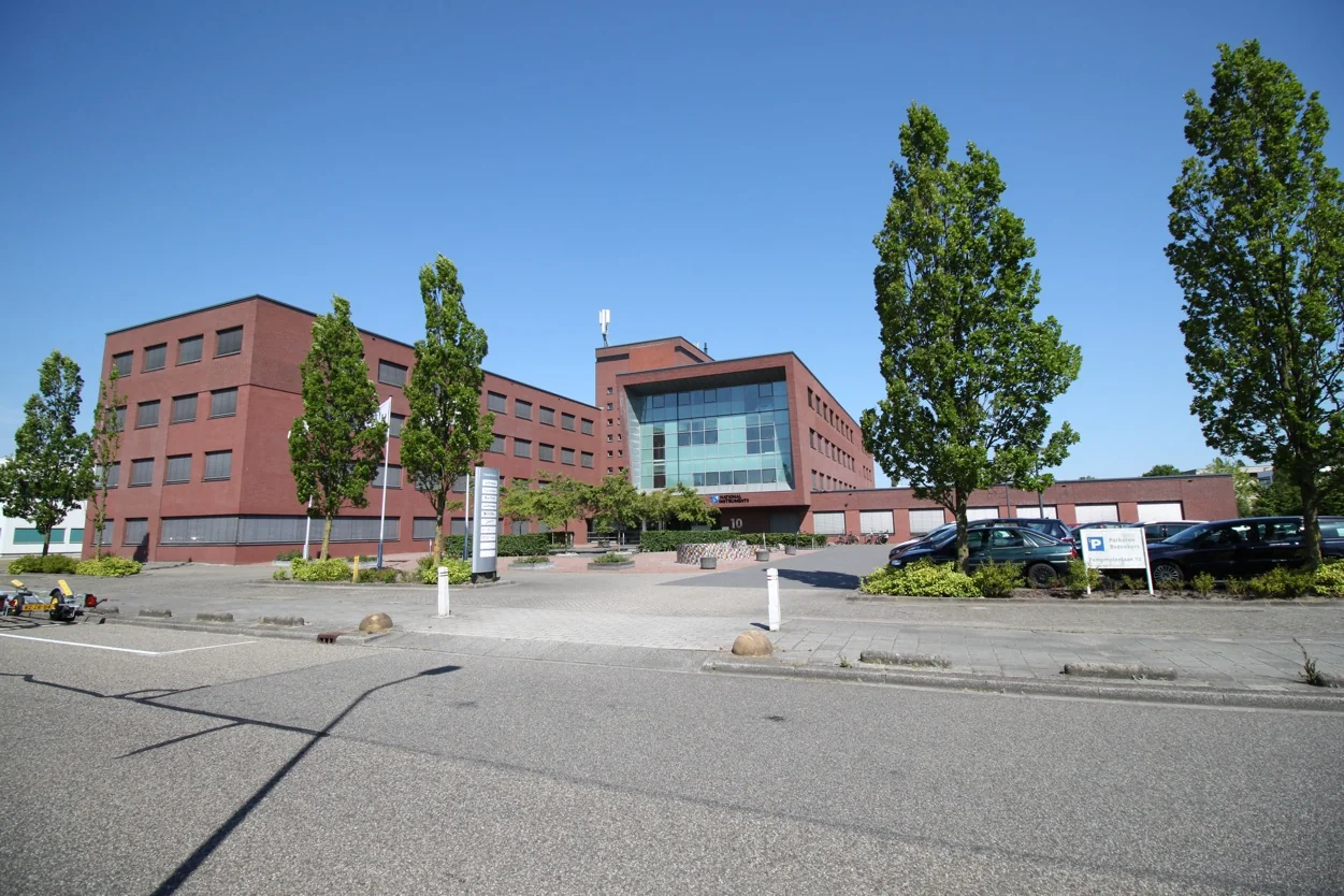 Modern kantoorgebouw aan de Pompmolenlaan met bakstenen gevel, grote ramen en omliggende parkeerplaatsen en bomen.