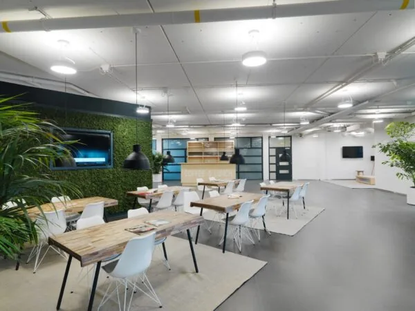 Moderne en lichte kantoorkantine aan de Pompmolenlaan met houten tafels, witte stoelen en een groene moswand.