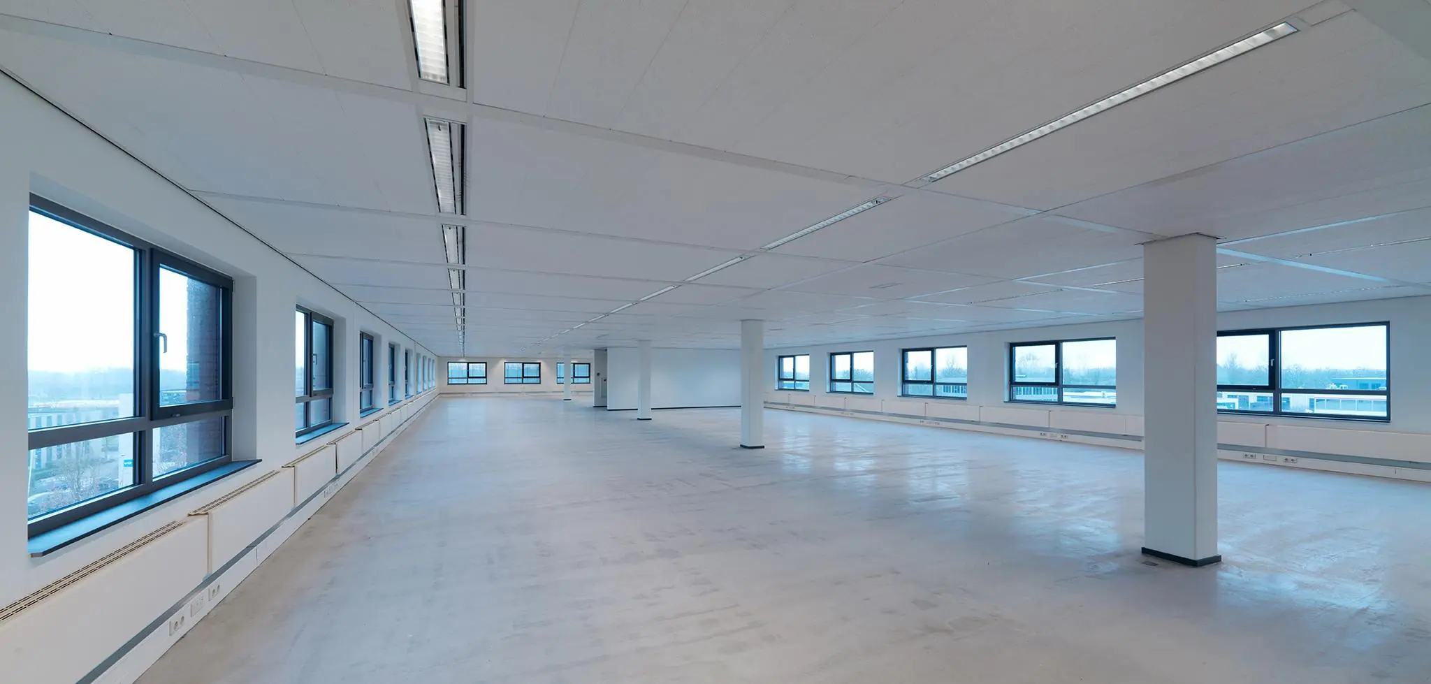 Lege, moderne kantoorruimte aan de Pompmolenlaan met grote ramen en een betonnen vloer.