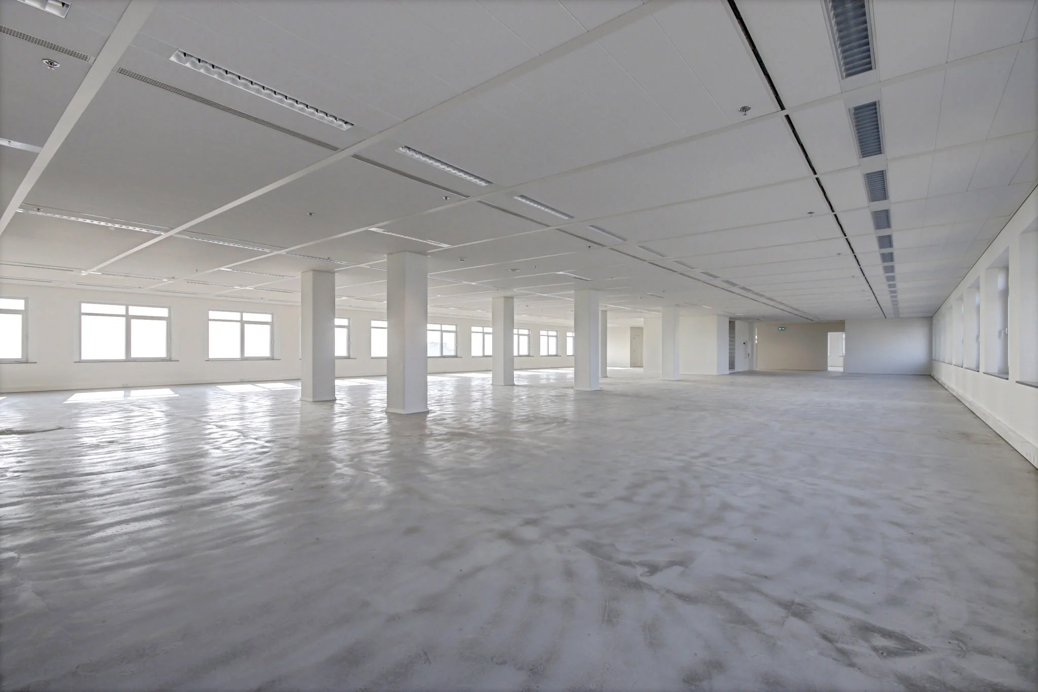 Leeg, licht en ruim kantoorinterieur aan de Winthontlaan met betonnen vloer en grote ramen.