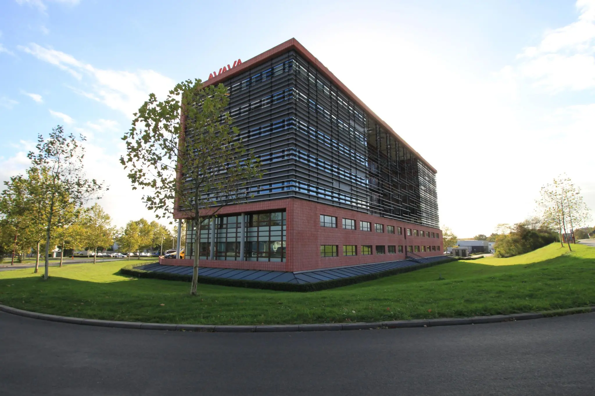 Modern kantoorgebouw aan de Marconibaan met rode gevel en horizontale zonwering, omringd door gras en bomen.