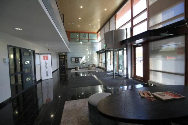 Moderne entreehal van een kantoorpand aan de Marconibaan met glazen draaideur, ontvangstruimte en bewegwijzering naar het notariaat.