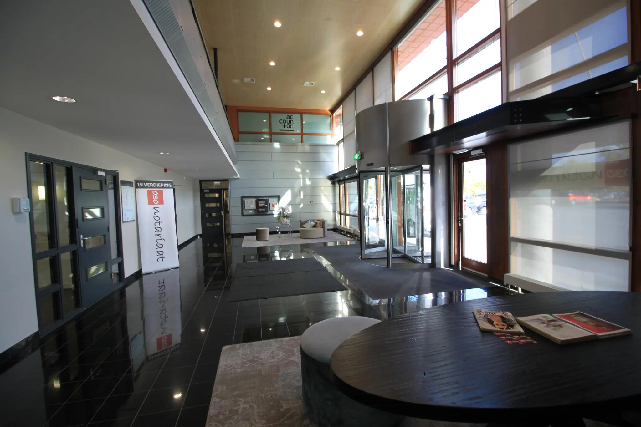 Moderne entreehal van een kantoorpand aan de Marconibaan met glazen draaideur, ontvangstruimte en bewegwijzering naar het notariaat.