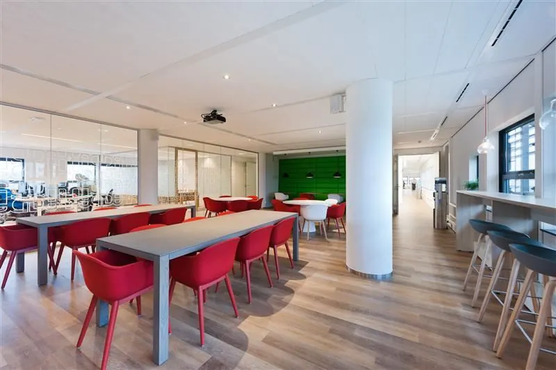 Moderne bedrijfsruimte aan de Marconibaan met houten vloer, rode stoelen en glazen vergaderruimtes.