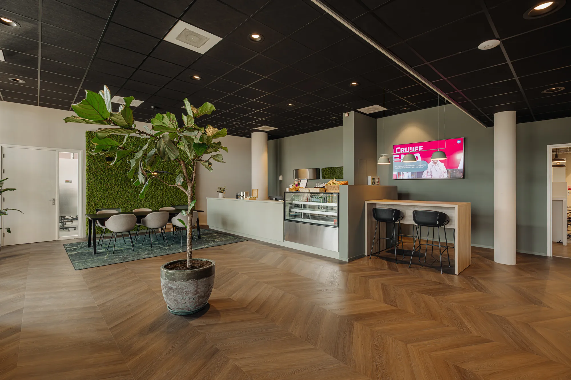 Een moderne lounge met een groene plantenmuur, een zitgedeelte, een toonbank met snacks en een tv-scherm aan de muur.