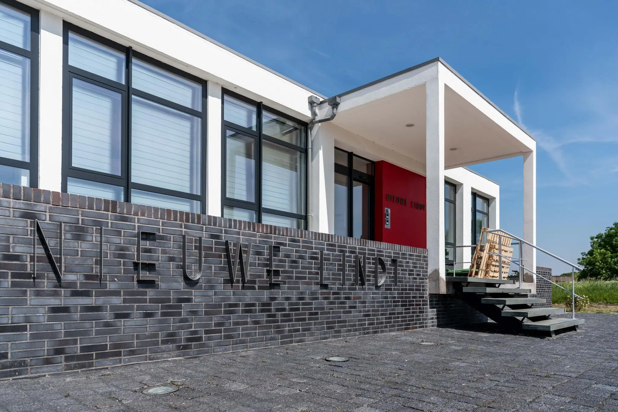 Moderne voorgevel van gebouw 'Nieuwe Lindt' met grote ramen en een rode entree.