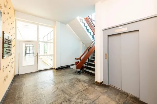 Ingangshal met trap, lift en glazen deur in een gebouw aan de Lindtsedijk.