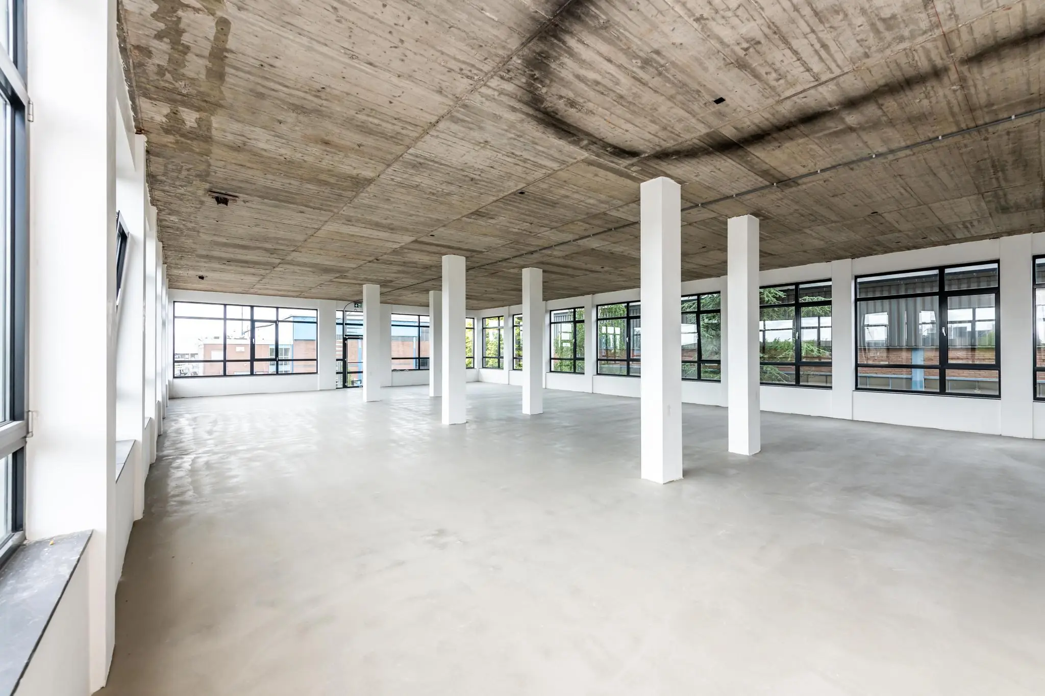 Leeg industrieel kantoorpand aan de Lindtsedijk met betonnen plafond, witte pilaren en grote ramen.
