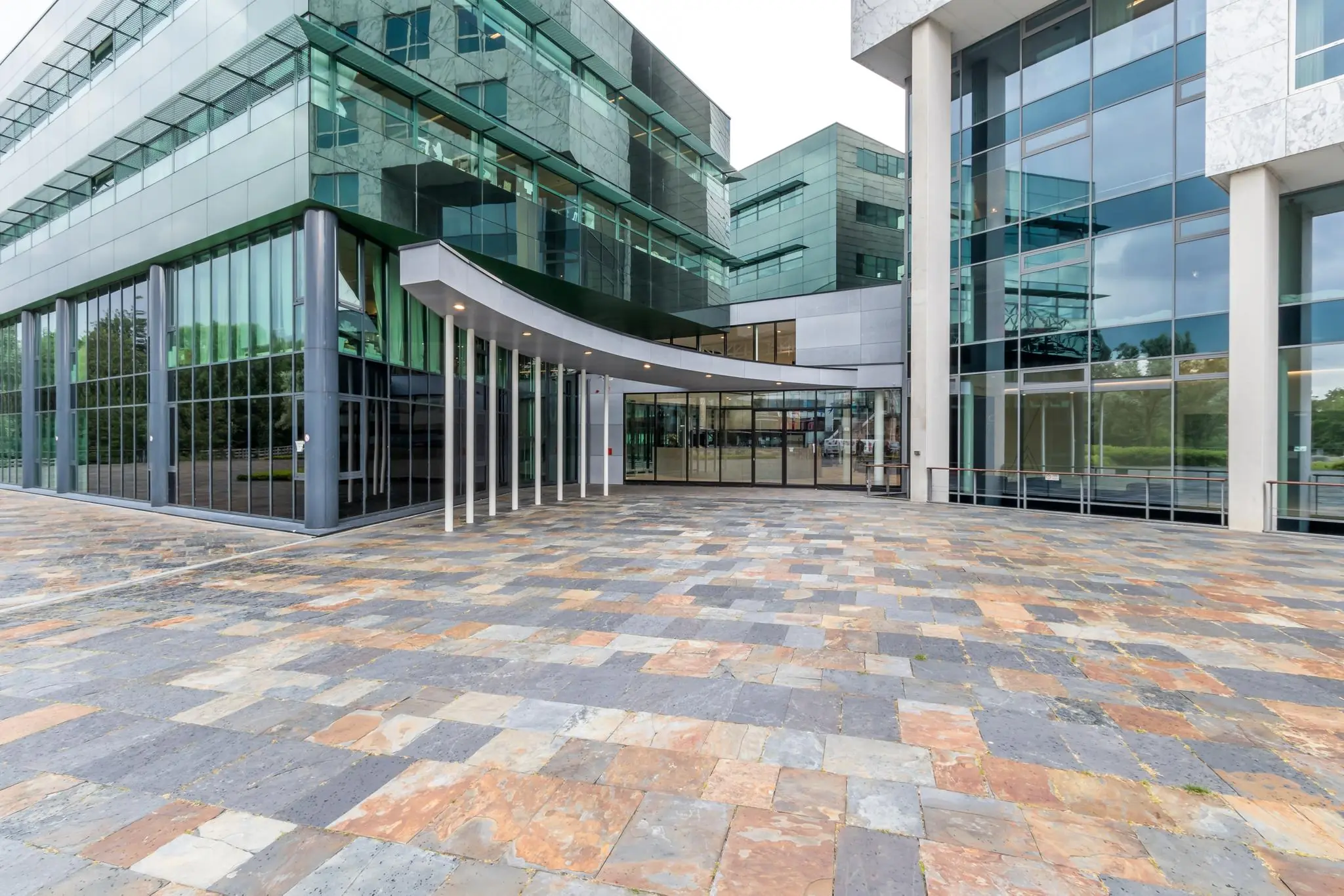 Moderne glazen entree van een kantoorgebouw op het Herculesplein met kleurrijk betegeld voorplein.