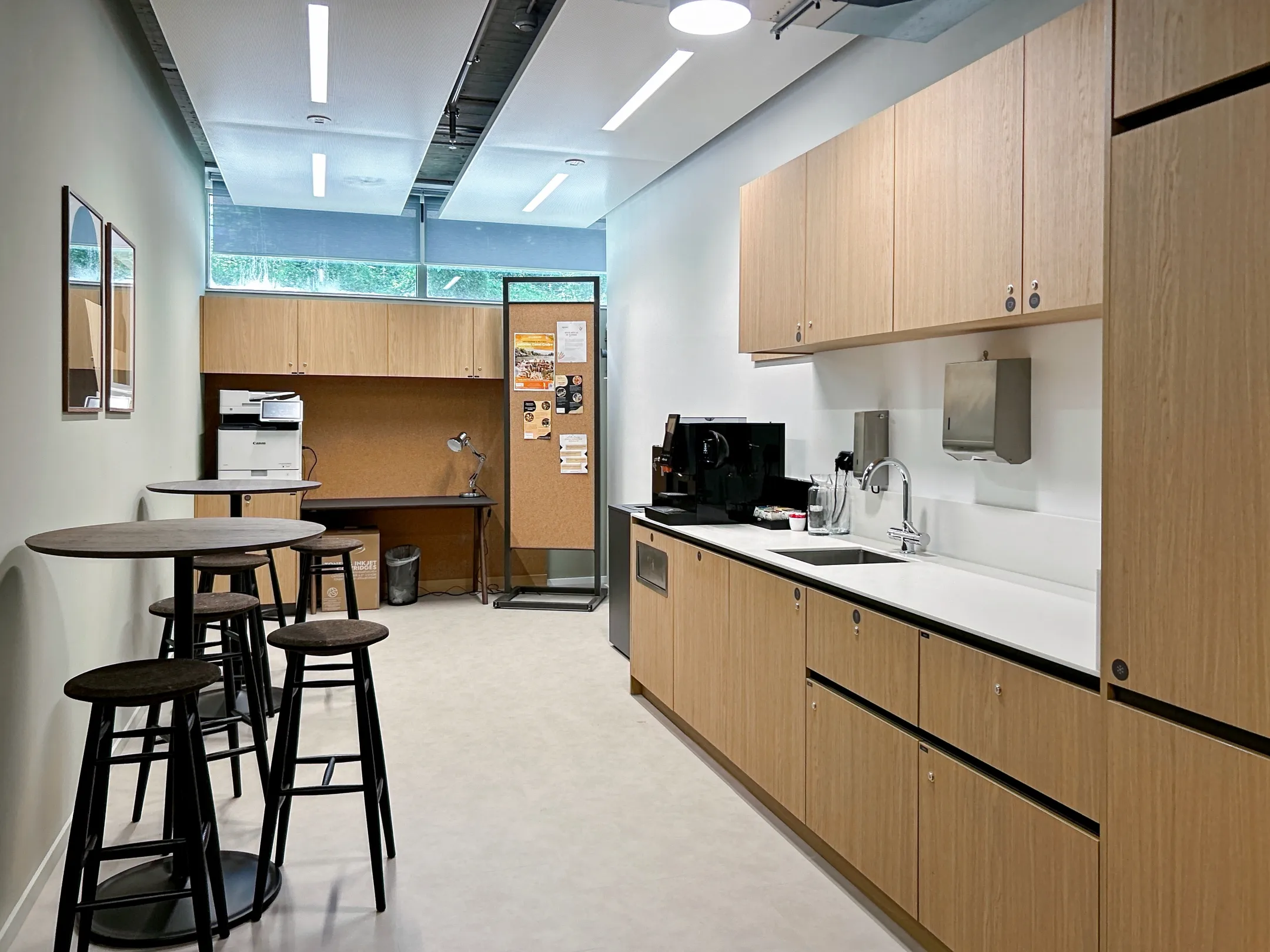 Moderne bedrijfskeuken met houten kasten, barkrukken en kantoorapparatuur.