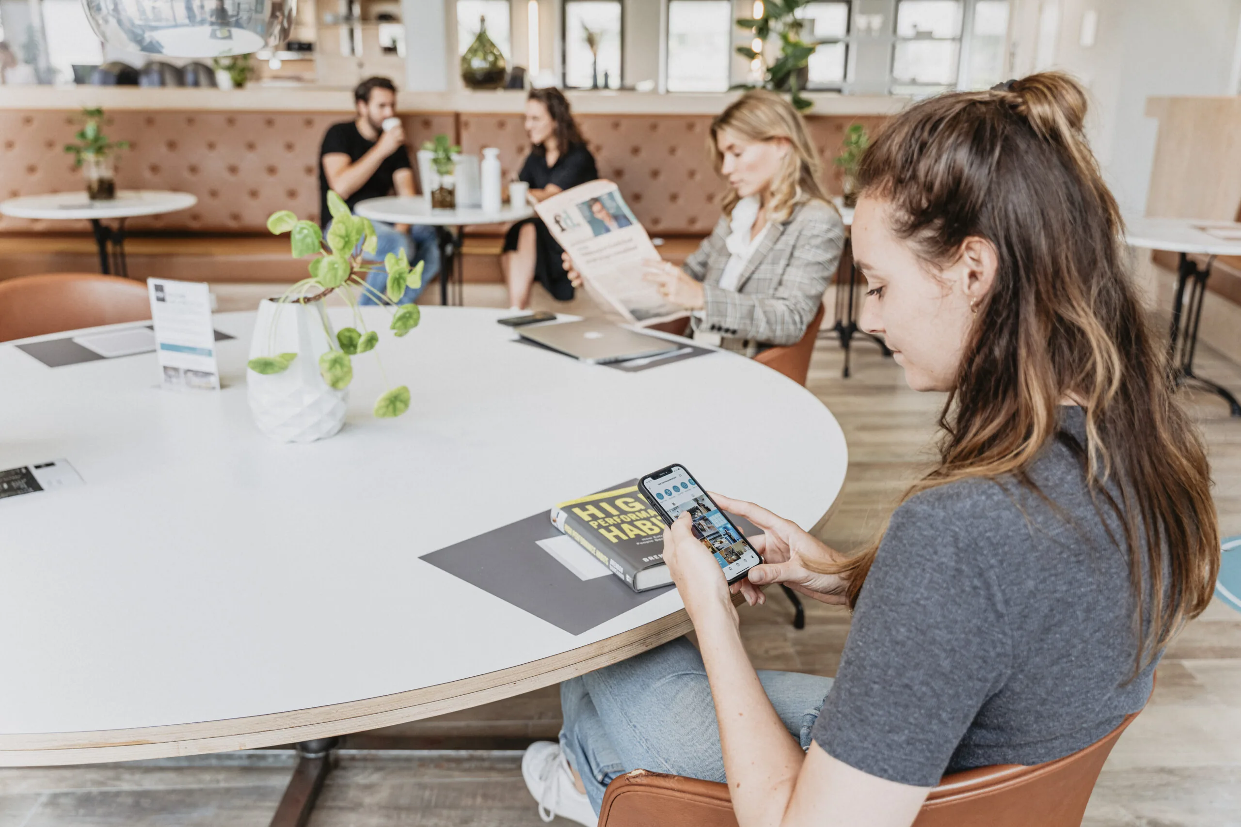 Vrouw bekijkt haar telefoon aan een ronde tafel in een moderne werk- of wachtruimte bij 7HNK Utrecht CS.