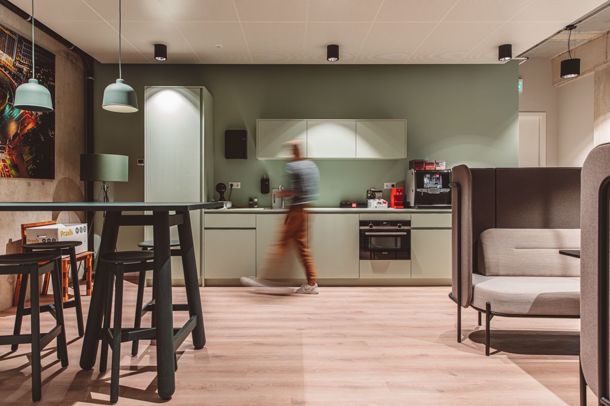 Een moderne keuken met een persoon die beweging vertoont voor een groen afgewerkte wand en kasten.