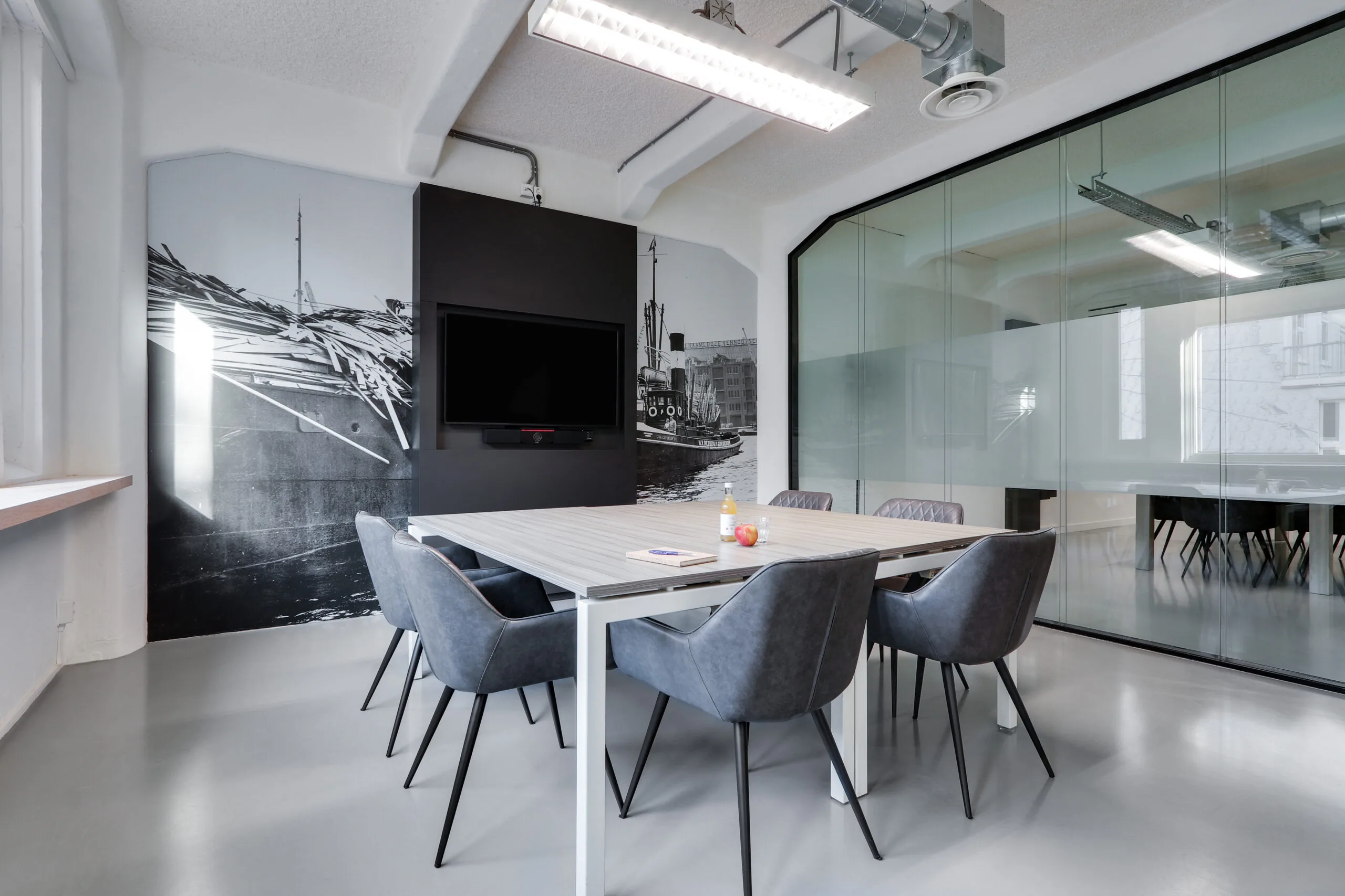 Moderne vergaderruimte in Amsterdam Houthavens met glazen wanden, een muurschildering van de haven en een tafel met zes stoelen.