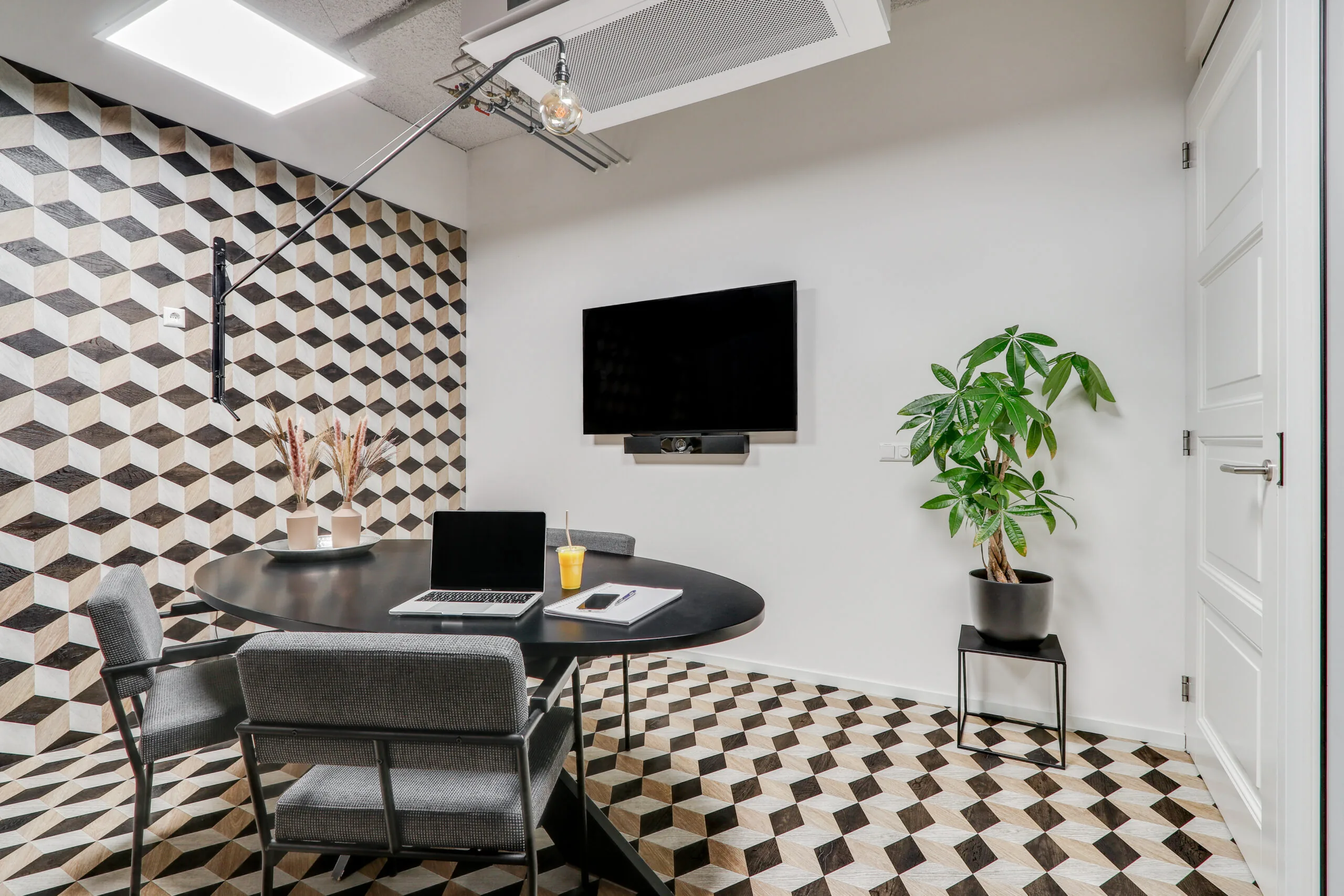Moderne vergaderruimte in Amsterdam Schinkel met geometrisch patroon op vloer en muur, ronde tafel, stoelen, tv-scherm en een groene plant.