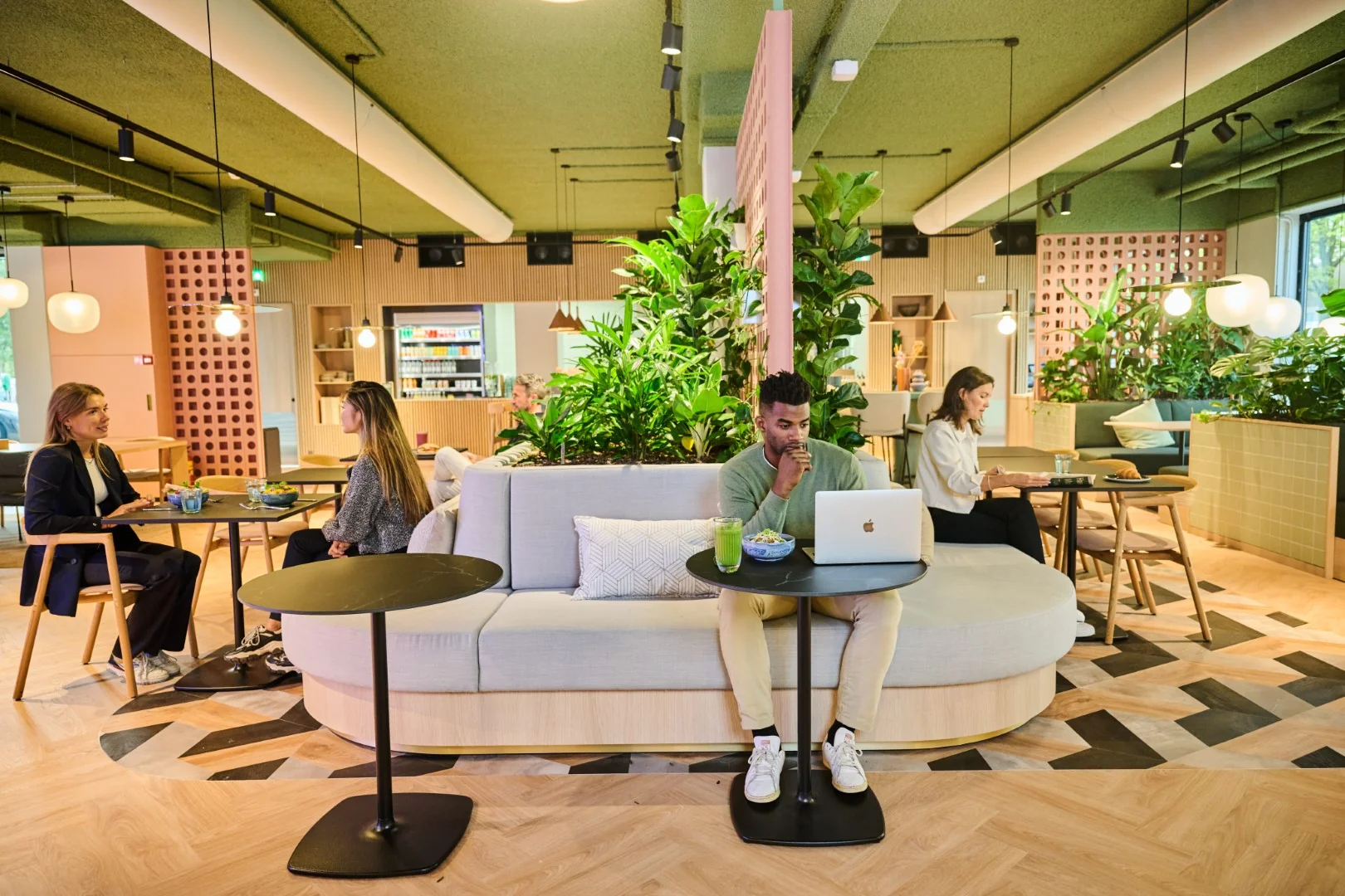 Mensen werken en overleggen in een modern, groen ingericht café met een ontspannen werksfeer.