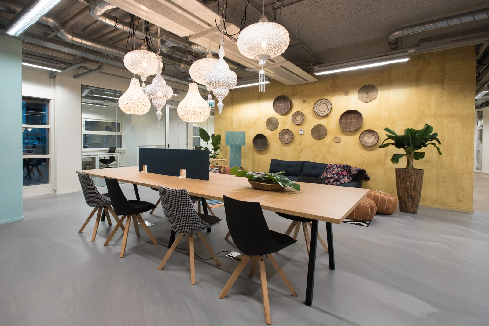 Moderne en sfeervol ingerichte werkruimte in HNK Amsterdam Zuidoost met lange houten tafel, designstoelen, hanglampen en decoratieve wandpanelen.