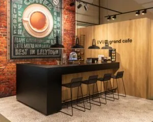 Moderne grand café-hoek met zwarte bar, hoge stoelen en een grote koffiekunstwand in kantoorruimte aan de Pascallaan 60-78 in Lelystad.
