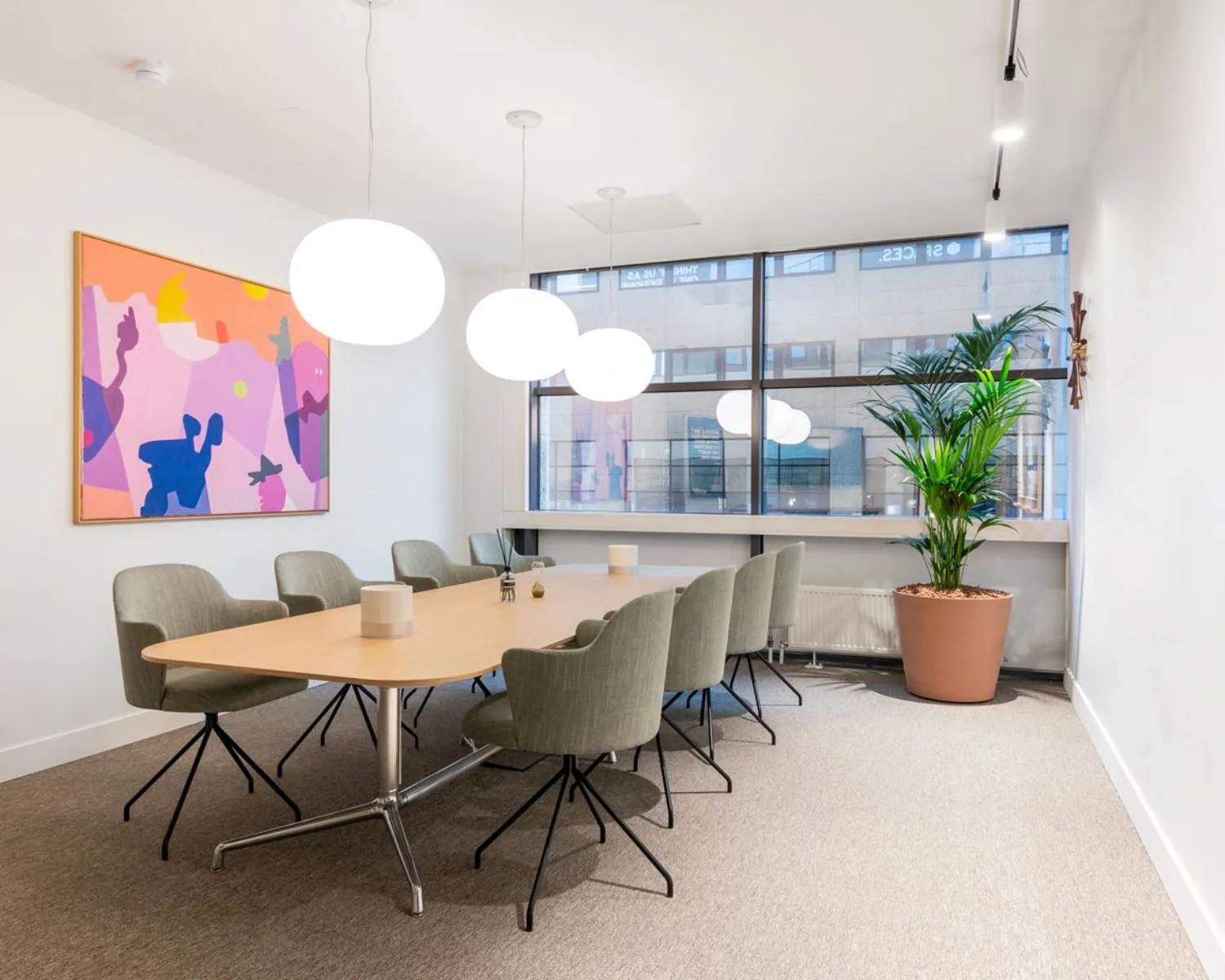 Vergaderruimte met een lange houten tafel, moderne stoelen, kleurrijk kunstwerk en grote ramen in kantoor aan Schimmelt 2-16 in Eindhoven.