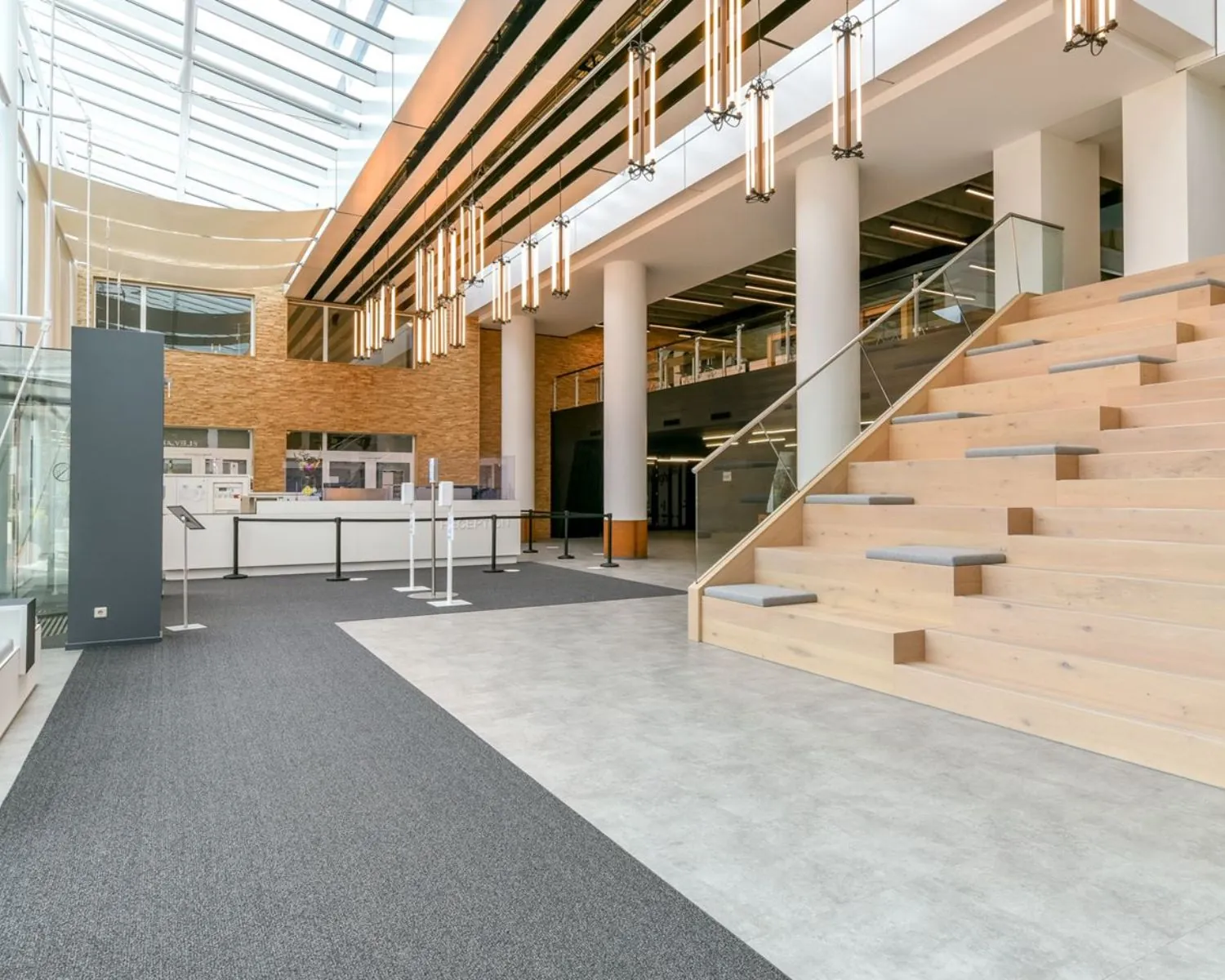 Moderne entreehal van het Coengebouw aan de Kabelweg 37 in Amsterdam met houten zittrappen, balie en glazen dak.