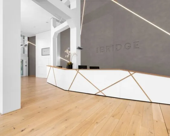 Moderne receptiebalie in de kantoorruimte "The Bridge" aan de JP Coenstraat in Den Haag met strakke witte en houten accenten.