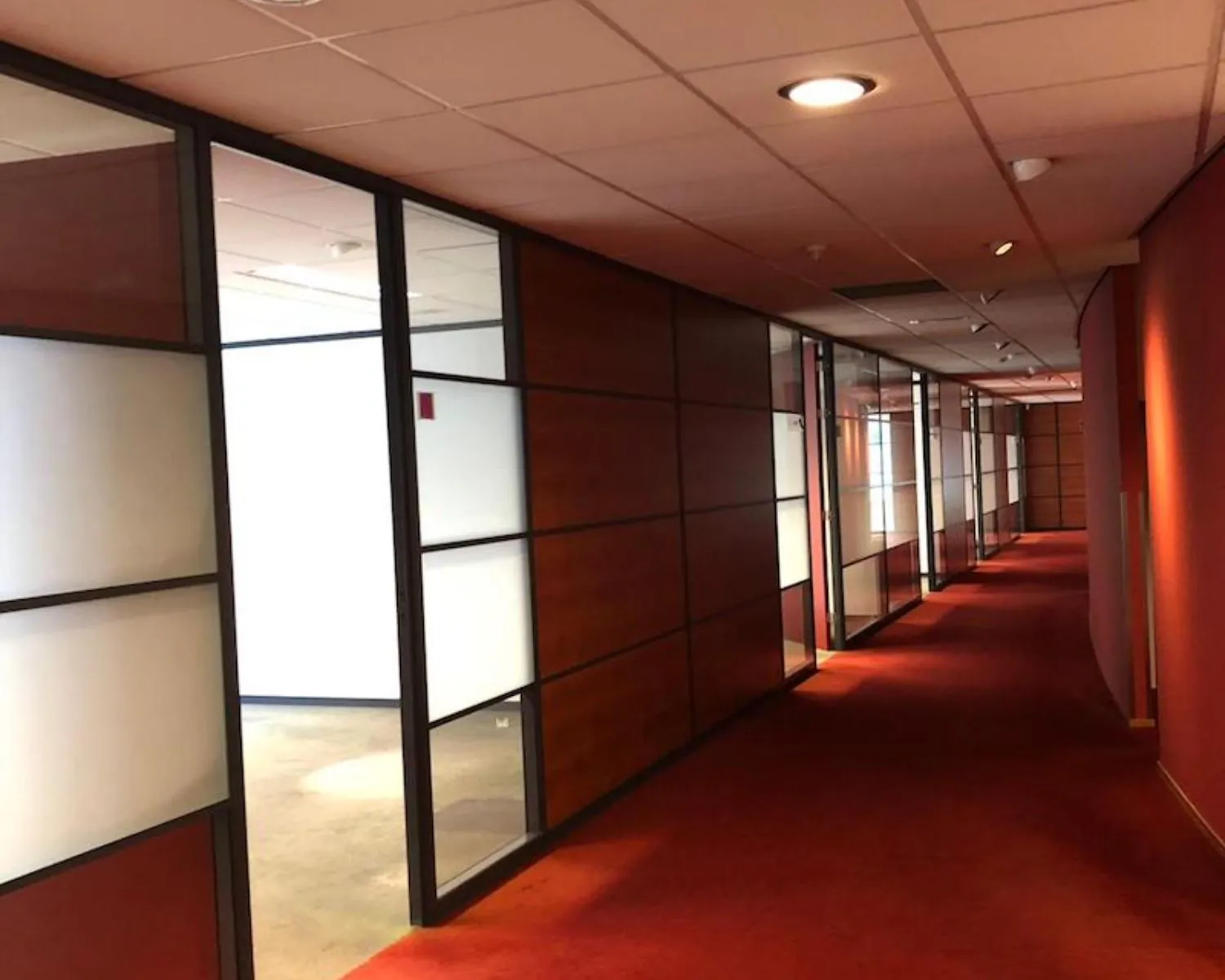 Gang met glazen kantoorwanden en rood tapijt in kantoorpand aan de Reeuwijkse Poort 114 in Reeuwijk.